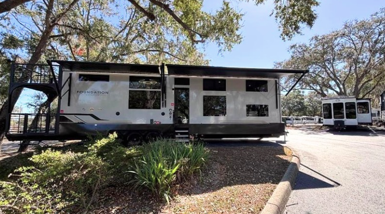 Large Foundation luxury travel trailer with rooftop balcony deck and expanded slide-outs parked at a wooded RV resort campsite