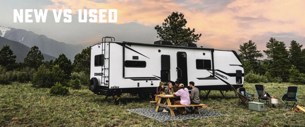 Travel trailer parked in a mountain campsite with people gathered around a picnic table, featuring text that reads “New vs Used.