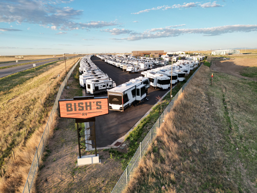 Aerial view of a Bish’s RV dealership lot filled with rows of travel trailers and fifth wheels beside a highway, featuring a large Bish’s RV roadside sign