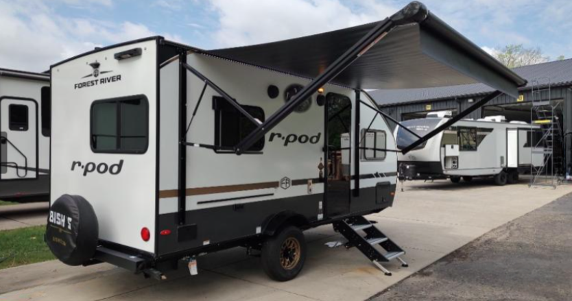 Forest River R-Pod travel trailer parked at an RV dealership with its power awning extended, showcasing the compact lightweight camper’s outdoor living space and modern exterior design.