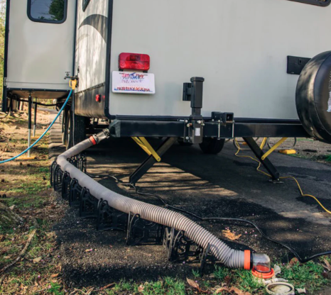 RV campsite sewer hookup setup showing a connected sewer hose supported by an elevated hose carrier system, ensuring proper waste drainage from a travel trailer to the campground sewer connection