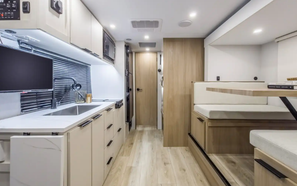 Modern RV interior featuring a residential-style kitchen with solid-surface countertops, large sink, ample cabinetry, and a booth dinette, creating an open and functional living space for travel and camping.