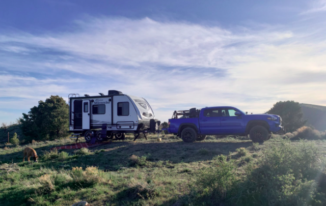 Compact travel trailer being towed by a midsize pickup truck at a scenic campsite, highlighting a lightweight, towable RV setup designed for adventure, off-grid camping, and easy travel.