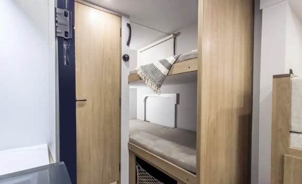 Compact RV bunk room featuring stacked bunk beds with safety rail, privacy curtain, built-in storage, and a space-efficient design that provides comfortable sleeping accommodations for kids or guests.
