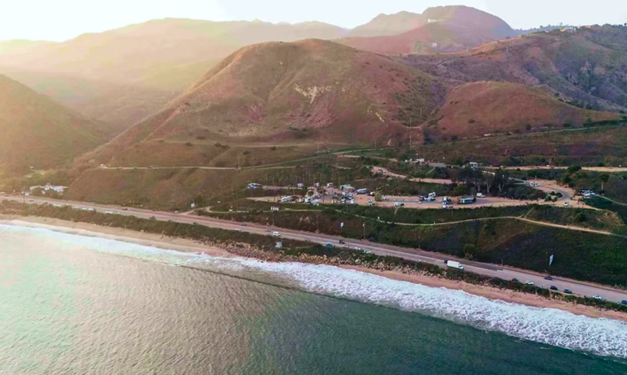 erial view of Surf Outpost RV Resort in Malibu, California, nestled between the Pacific Ocean and the scenic Santa Monica Mountains. The image showcases the resort’s unique bluff-top location, offering campers sweeping coastal views, beach access, and a picturesque Southern California camping experience