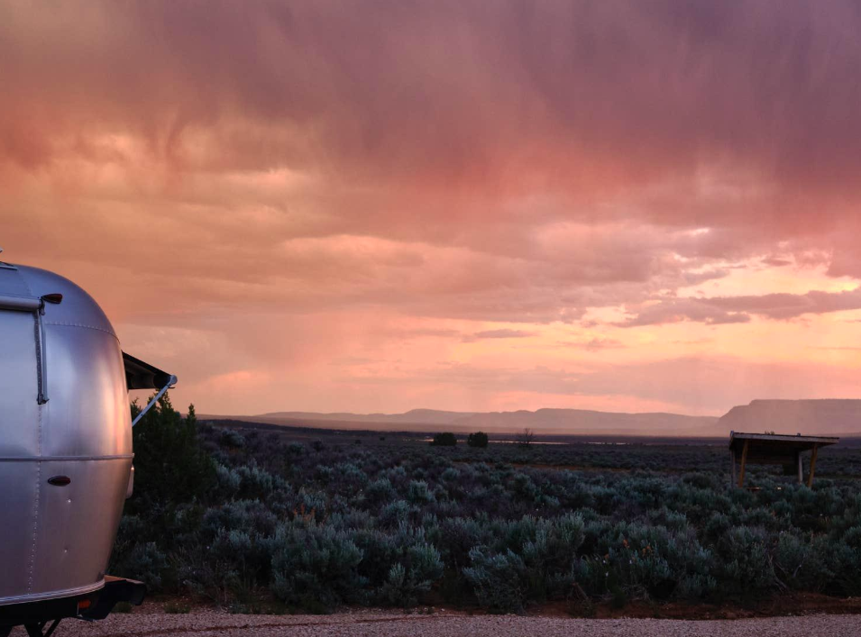 Travel trailer campsite at sunset overlooking a wide desert landscape, with dramatic storm clouds and colorful skies creating a scenic backdrop for RV camping and outdoor adventure
