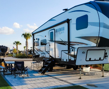 Luxury fifth wheel RV parked on a premium concrete campsite at a coastal RV resort. The spacious site features outdoor seating, full hookups, landscaped surroundings, and easy access to resort amenities, offering a comfortable and upscale RV camping experience
