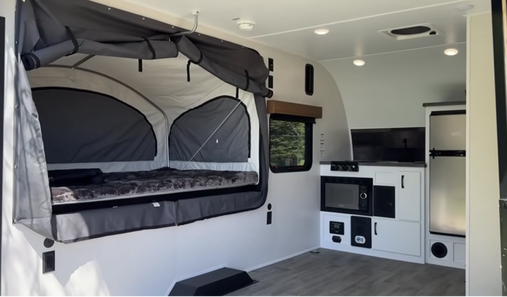 Modern Buggy Hopper travel trailer interior featuring a fold-out canvas bunk system, open living space, entertainment center, microwave, refrigerator, and compact kitchen amenities. The innovative design blends the comfort of a travel trailer with the open-air camping experience of a tent camper, creating a versatile and adventure-ready RV for outdoor enthusiasts