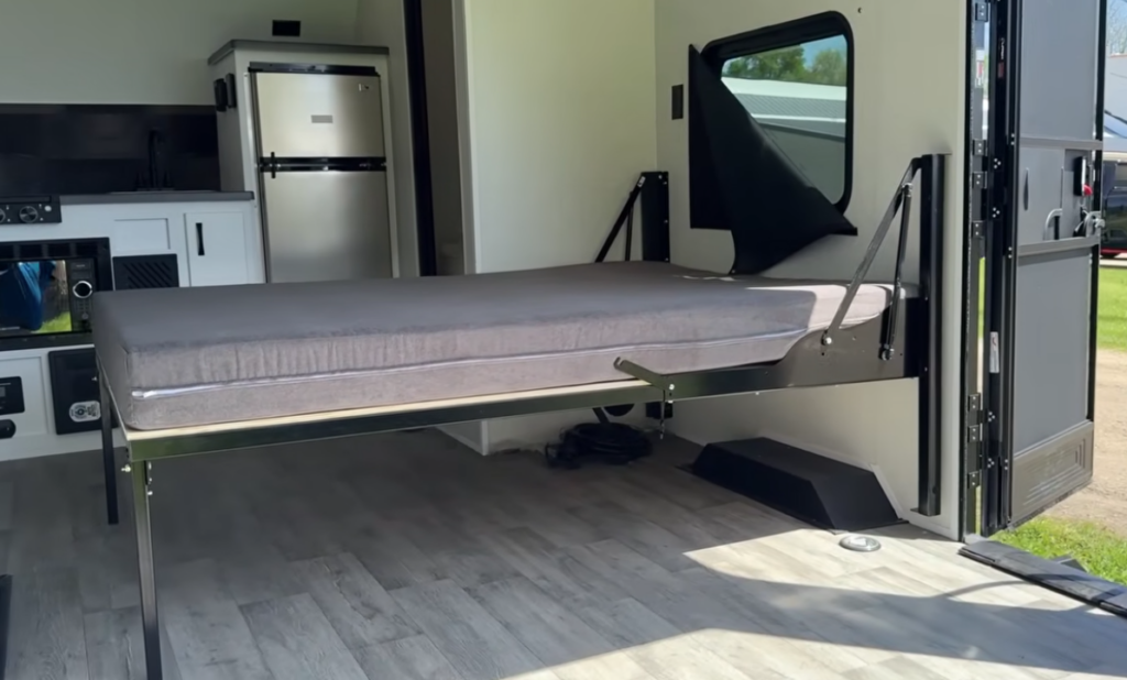 Innovative fold-down bed system inside the Modern Buggy Hopper travel trailer, creating a spacious sleeping area that extends through the rear cargo-style opening. This versatile design transforms the compact RV into a roomy bedroom while maximizing interior living space, making it ideal for adventurous travelers seeking comfort in a lightweight, easy-to-tow camper