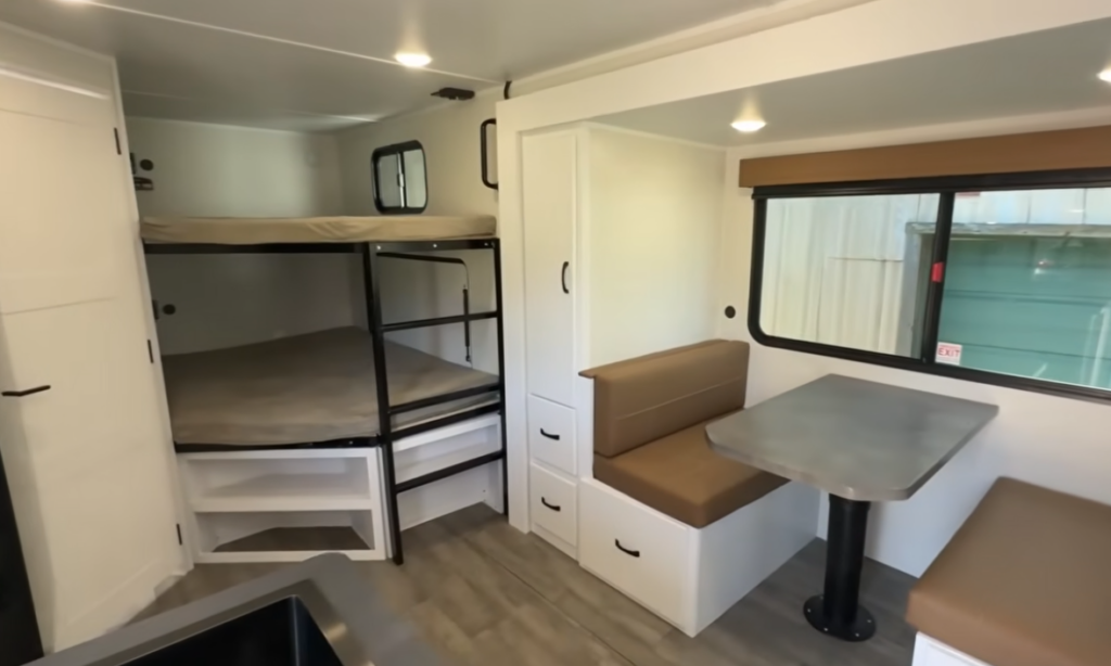 Family-friendly interior of the Modern Buggy Hopper travel trailer featuring double bunk beds, a booth dinette with built-in storage, overhead cabinetry, and a bright open floorplan. The efficient layout maximizes sleeping capacity, dining space, and storage, making this lightweight adventure-ready RV ideal for families, couples, and outdoor enthusiasts seeking comfort in a compact camper
