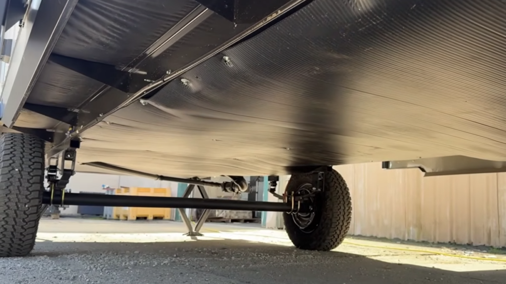 Underside view of the Modern Buggy Hopper travel trailer highlighting its fully enclosed and insulated underbelly, rugged axle system, and off-road-ready suspension components. Designed for durability and all-season camping, the protected undercarriage helps shield plumbing and essential systems while supporting travel on a variety of road and terrain conditions