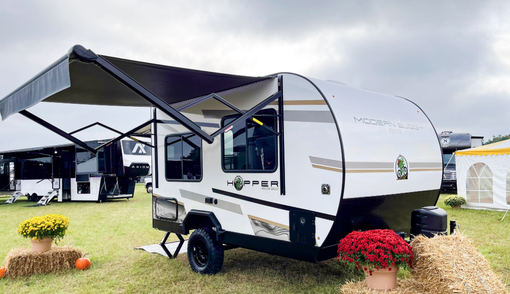 Modern Buggy Hopper travel trailer displayed outdoors with an extended power awning, rugged off-road tires, and compact lightweight design. Built for adventurous travelers, this small towable RV combines modern styling, outdoor-ready features, and easy towing for weekend camping trips and off-grid exploration.