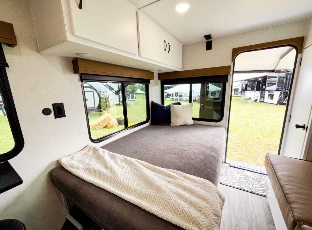 Convertible rear sleeping area inside the Modern Buggy Hopper travel trailer featuring a spacious bed setup, large panoramic windows, overhead storage cabinets, and direct access to the campsite through the rear entry door. The flexible layout maximizes comfort, natural light, and functionality in a compact adventure-ready RV.