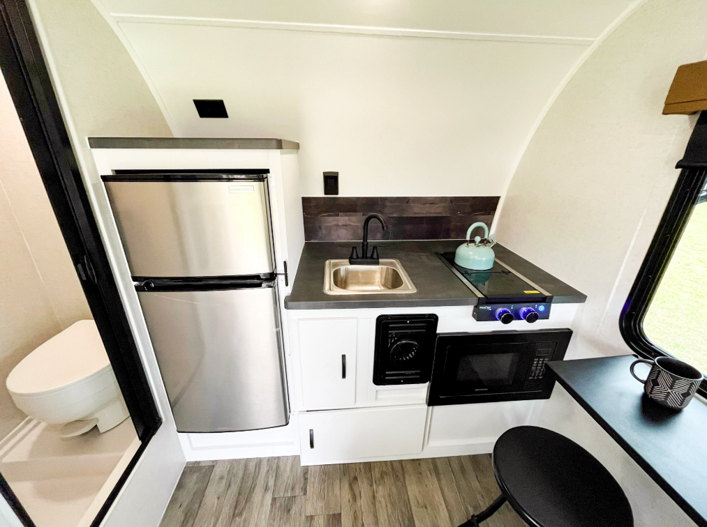 Compact kitchen and bathroom layout inside the Modern Buggy Hopper travel trailer featuring a residential-style refrigerator, stainless steel sink, cooktop, microwave, storage cabinets, and a private wet bath. The efficient floorplan maximizes functionality and comfort while maintaining a lightweight, easy-to-tow design for adventurous RV travelers