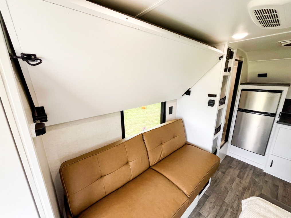 Modern Buggy Hopper travel trailer interior featuring a jackknife sofa beneath a fold-down upper bunk bed, creating a versatile multi-use living and sleeping space. The compact design maximizes seating, sleeping capacity, and functionality while maintaining an open, lightweight layout ideal for adventure-focused RV travel.