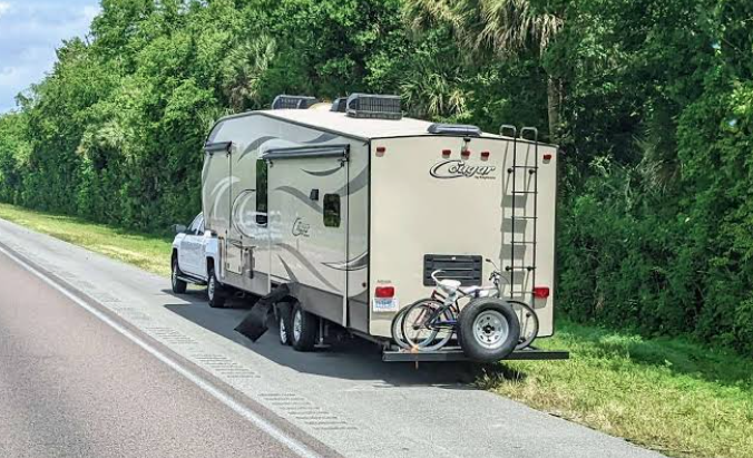Travel trailer pulled over safely on the shoulder of a highway after an apparent roadside issue. The RV remains connected to the tow vehicle with bicycles mounted on the rear rack, illustrating the importance of emergency preparedness, routine RV maintenance, and knowing how to safely handle unexpected roadside situations while traveling