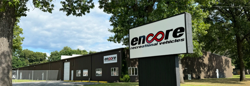 Encore Recreational Vehicles manufacturing facility with the company sign displayed prominently outside the production building. The facility represents the home of innovative RV manufacturing, where lightweight travel trailers and modern campers are designed and built with a focus on quality craftsmanship, durability, and adventure-ready performance
