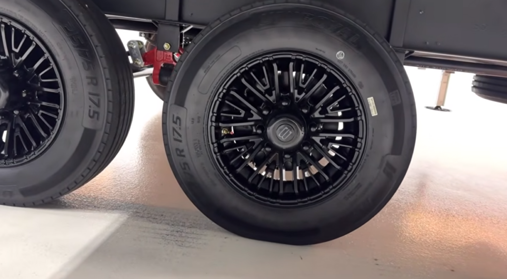 Close-up of a luxury fifth wheel's tandem axle featuring premium black aluminum wheels, heavy-duty RV tires, and upgraded suspension components.