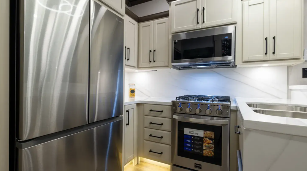 Luxury fifth wheel kitchen with a full-size residential refrigerator, stainless steel gas range and oven, microwave, solid-surface countertops, farmhouse-style sink, and abundant cabinetry. Designed for full-time RV living, the upscale kitchen combines premium appliances, generous storage, and residential comfort, making meal preparation easy during extended RV travel and camping adventures.