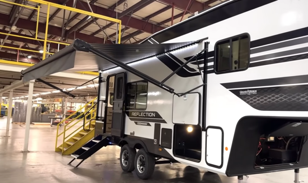 Exterior view of the Grand Design Reflection fifth wheel with its large power awning fully extended, creating a spacious outdoor living area.