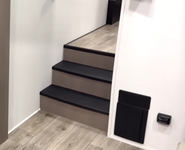 Wide, residential-style staircase inside a luxury fifth wheel leading from the main living area to the raised bedroom and bathroom.