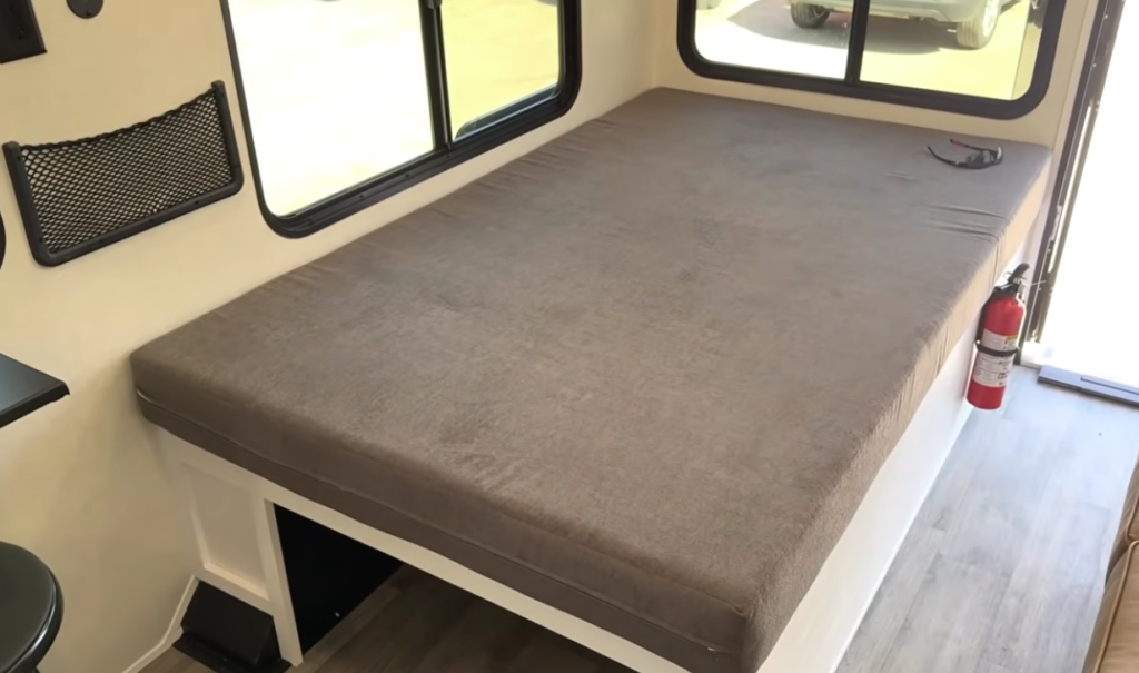 Spacious rear bed inside the Modern Buggy Hopper travel trailer featuring a large sleeping platform surrounded by panoramic windows for abundant natural light and campsite views.